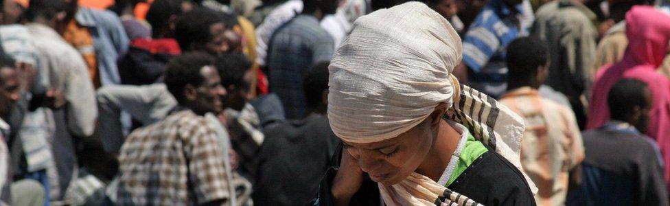 A woman walks past some 355 Would-be immigrants from Eritrea after their arrival by boat in the port of Italy's southern island of Lampedusa late on 21 August 2008.