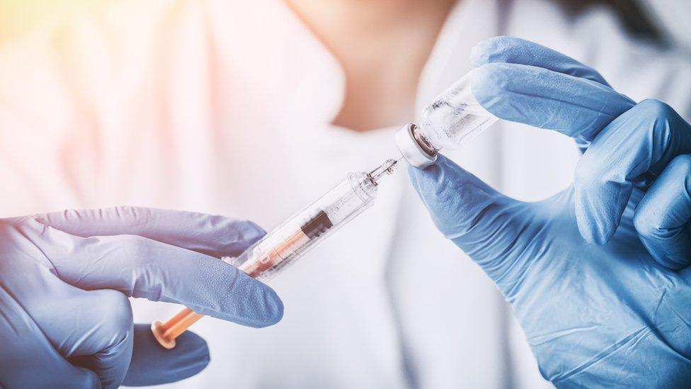 Hands in medical gloves fill a syringe from a small vial.