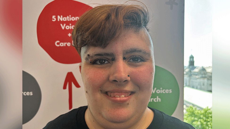 Headshot of Georgia who has short, reddish/brown hair and facial piercings. She is smiling and looking slightly off camera.
