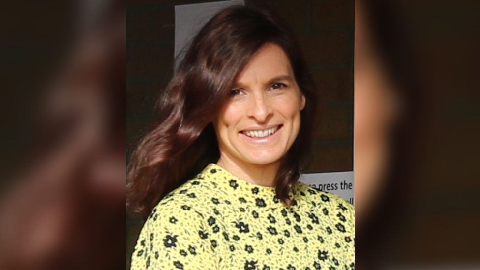 A close up shot of Joanne Hall, wearing a yellow and black outfit. She has brown hair and brown eyes.