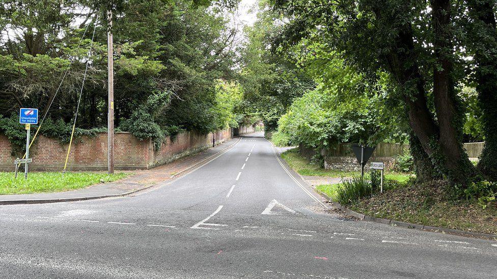 Road junction with crick wall along a leafy lane and a wooden fence along the right hand side