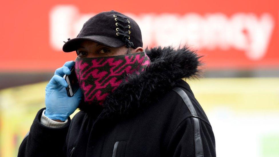 A man wearing a mask and latex gloves, on the phone outside a pharmacy