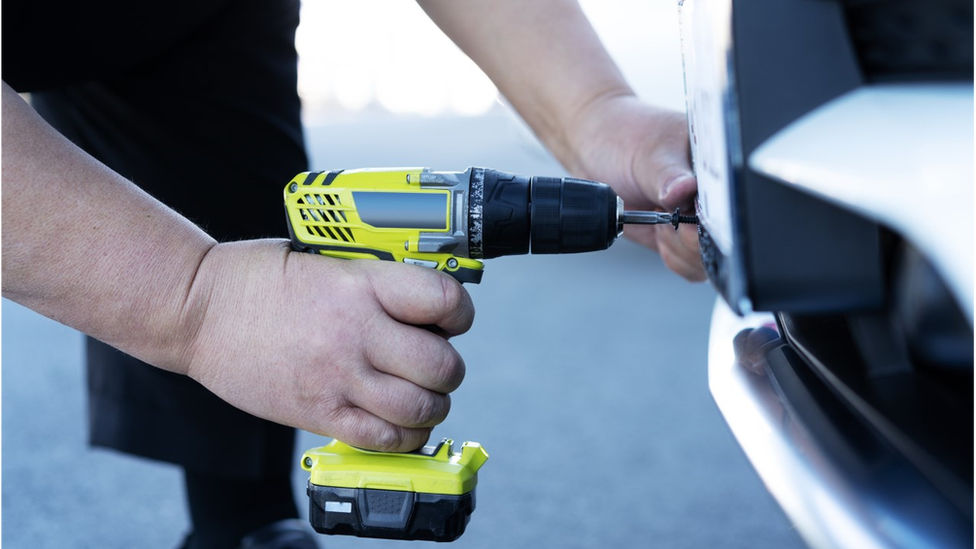 Man using drill to attach number plate to a car