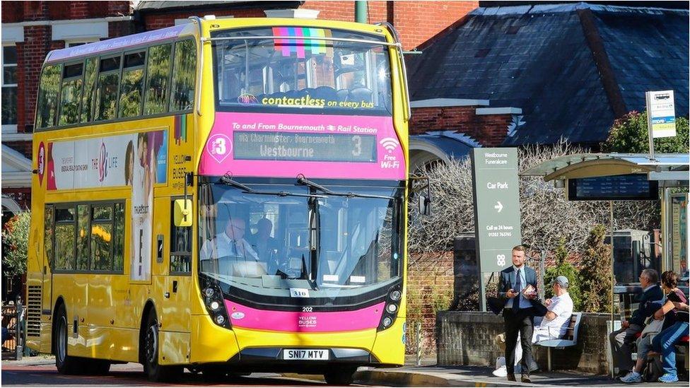 Yellow double-decker bus next to a bus stop with people waiting