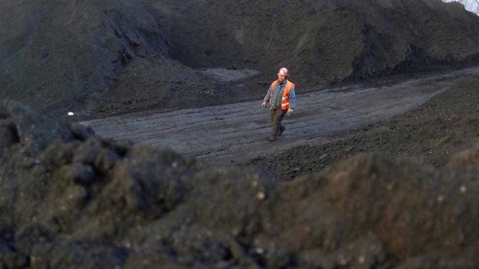 A worker walks past coal piles at a coal coking plant in Yuncheng, Shanxi province