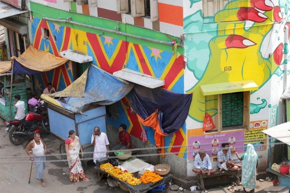 Indian commuters walk past a painted wall at Sonagachi red light district in Kolkata