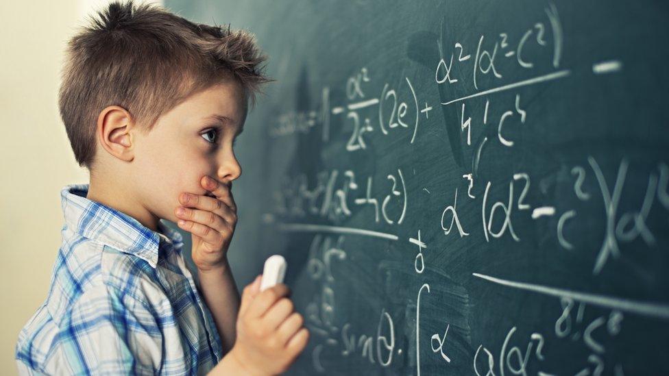 Stock photo of little boy solving a maths problem on a blackboard