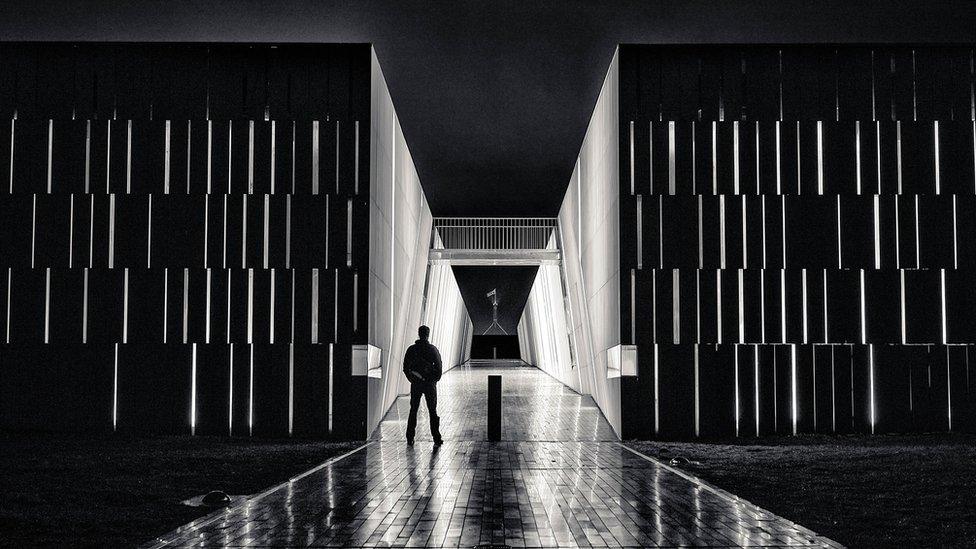 A black and white picture of a man framed against an open-air tunnel and the Australian Parliament House in the background