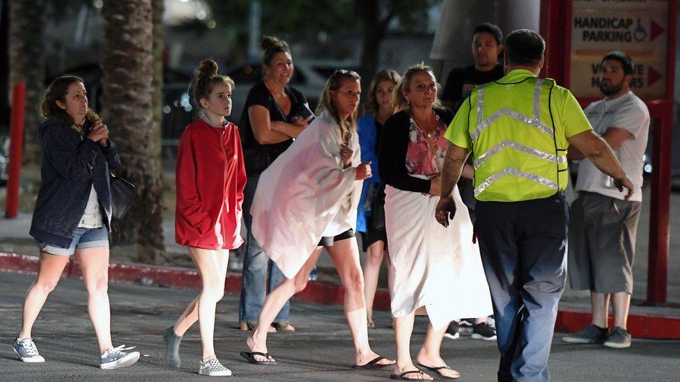 People, some with sheets around them, being directed by a man in a high-vis jacket