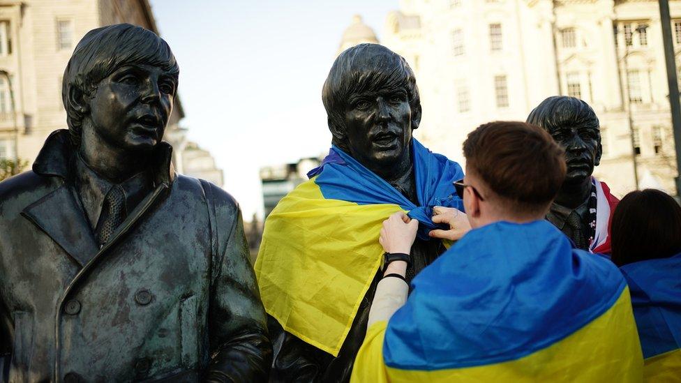 Man putting an Ukrainian flag on the Beatles Statue at Pier Head in Liverpoo