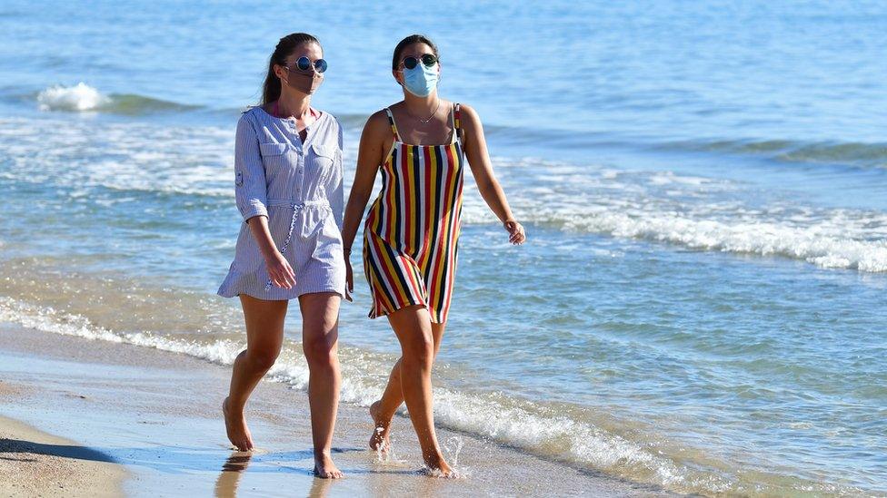 Women walking on a beach wearing face masks in Pensacola, Spain