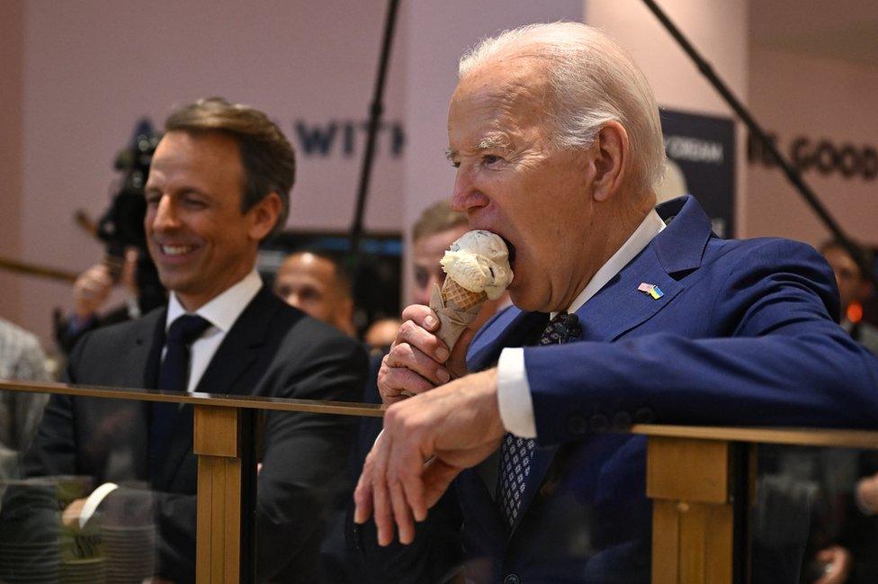 US President Joe Biden, flanked by host Seth Meyers, eats an ice cream cone at Van Leeuwen Ice Cream after taping an episode of Late Night with Seth Meyers in New York City on 26 February 2024