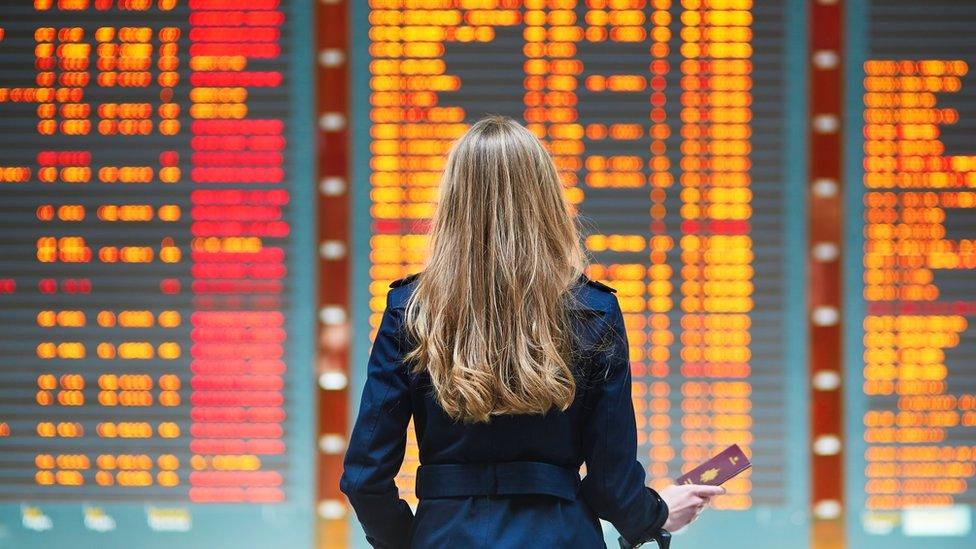 Stock image of the back of a woman looking at departure board in airport with her passport