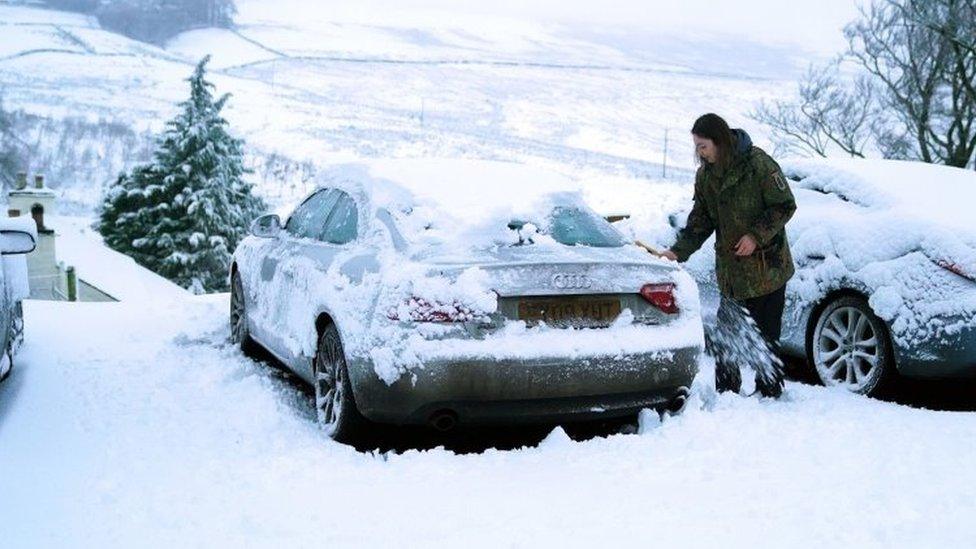 A motorist clears heavy overnight snow from a car in Carrshield in the Pennines, near Hexham in Northumberland