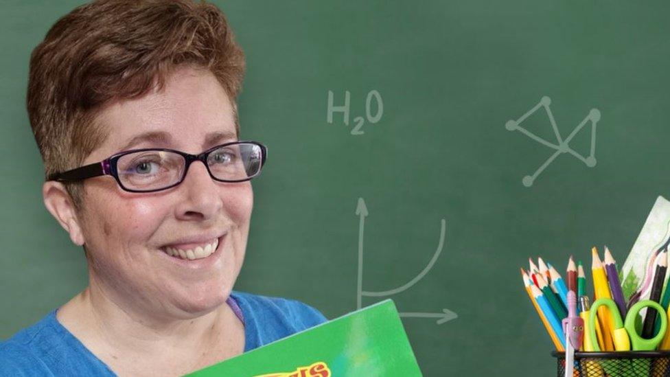 Lucy Chillery-Watson looks into the camera, wearing glasses and a blue top in front of a school board background