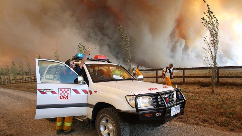 A group of firefighters and their vehicle in front of a towering fire on Black Saturday