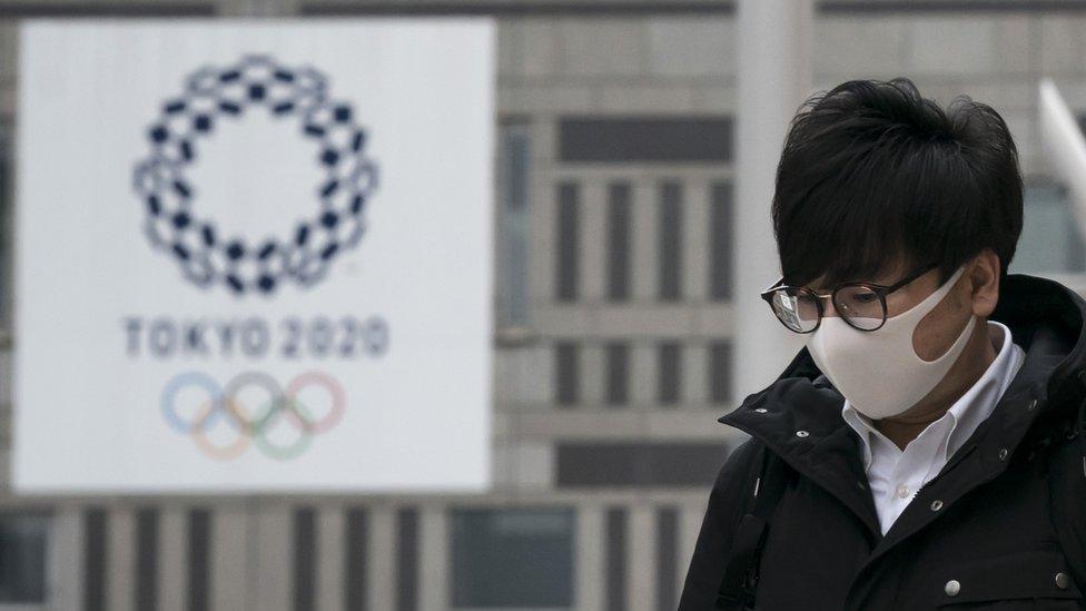 A pedestrian wearing a face mask walks past a banner promoting the upcoming Tokyo 2020 Olympic and Paralympic Games outside the Tokyo