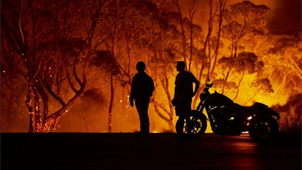 Residents look on as flames burn through bush on January 04, 2020 in Lake Tabourie, Australia