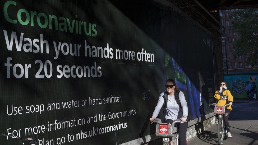 People cycle past a government coronavirus advert in London