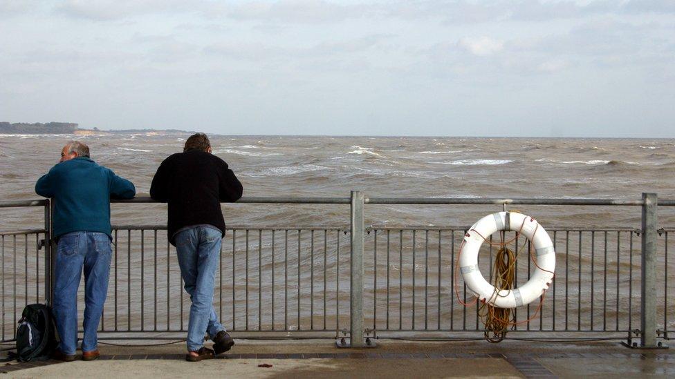 Two men looking over a fence towards the sea