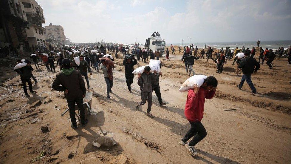 Palestinians carry bags of flour they took from an aid convoy