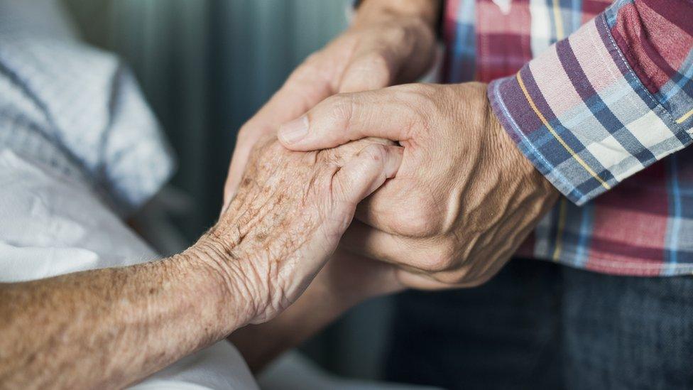 Man holding father's hand in hospital