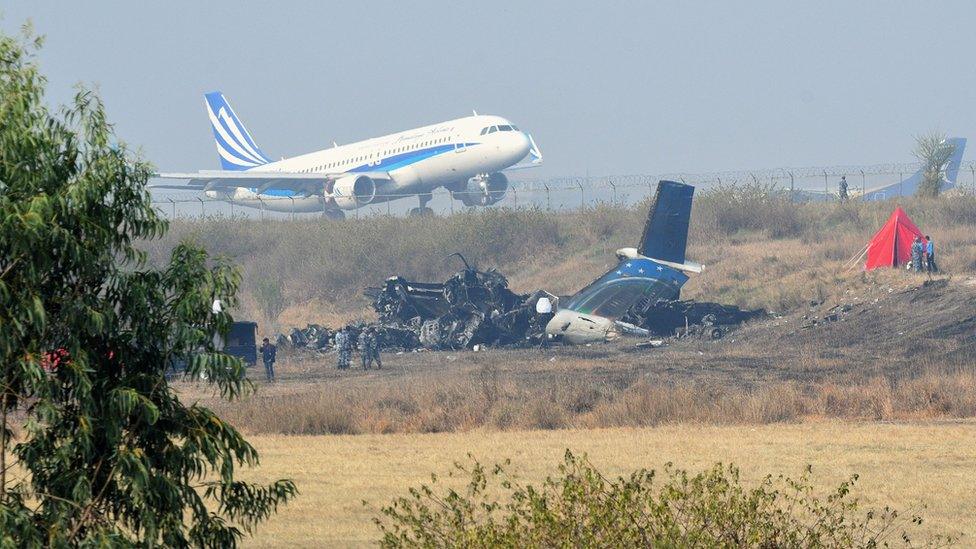 An airplane takes off at the international airport in Kathmandu on March 13, 2018, near the wreckage of a US-Bangla Airlines plane that crashed on March 12. At least 49 people were killed and 22 injured when a Bangladeshi plane crashed and burst into flames near Kathmandu airport on March 12, in the worst aviation disaster to hit Nepal in years.