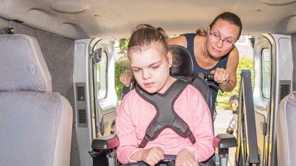 a girl in a wheelchair being pushed into a minibus by a mid-life woman, possibly her mum