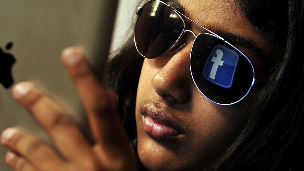 The Facebook logo reflected in the shades of a young Indian girl