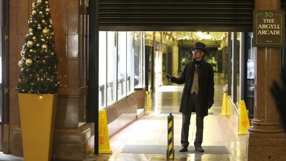 A doorman watches as the shutters come down at the Argyll Arcade in Glasgow as the new restrictions come into place