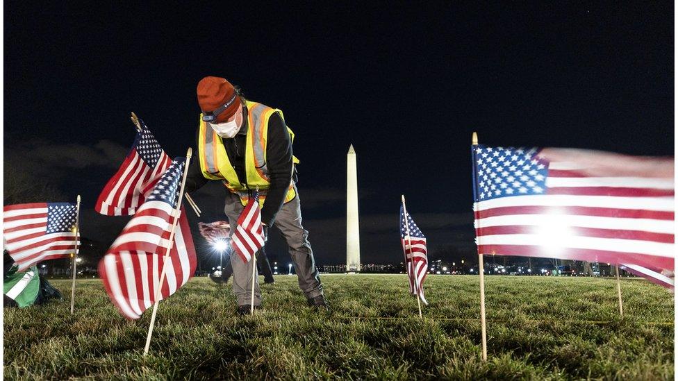 A worker plants several USA flags in the ground before the Washington Monument.