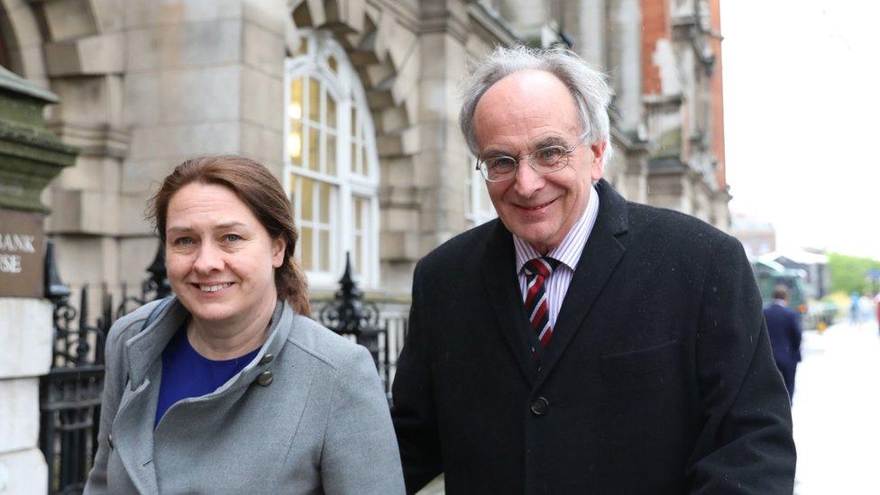 Woman with dark hair wearing grey coat and man with grey hair and glasses wearing dark coat and tie