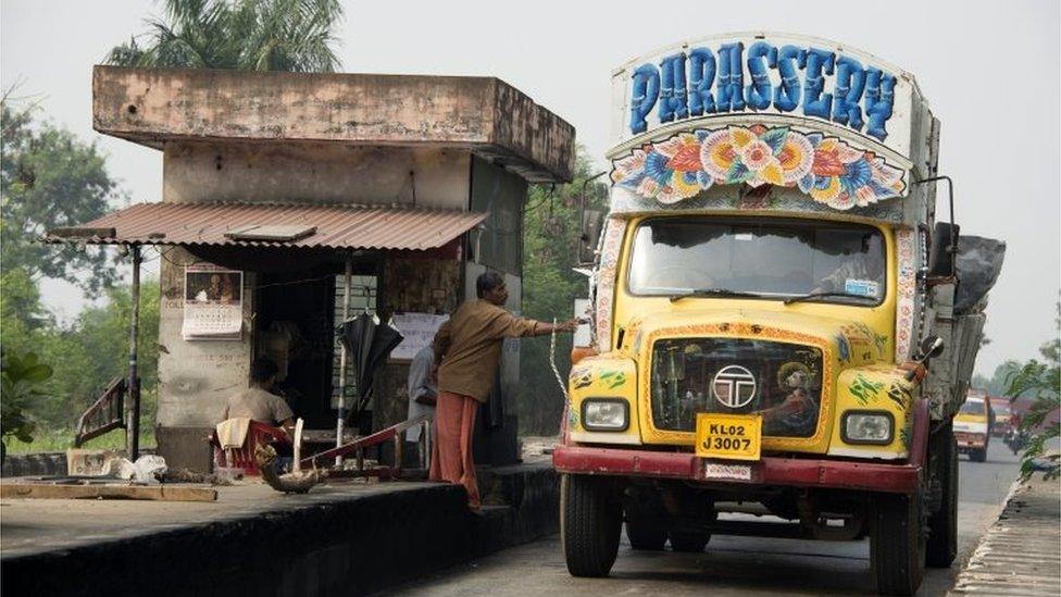 A lorry driver in his personalised hand-painted yellow Tata Semi-Forward Cab 1210SE Truck stops at a road toll in Kochi, Kerala, India.