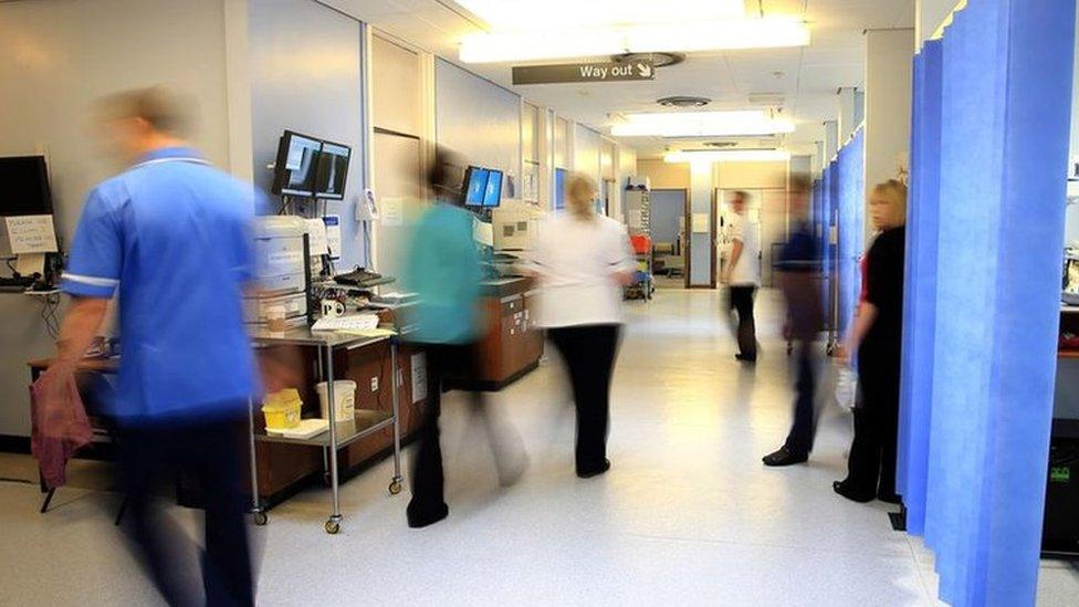 Staff in blue scrubs on a NHS hospital ward. They are slightly blurred because they are moving quickly