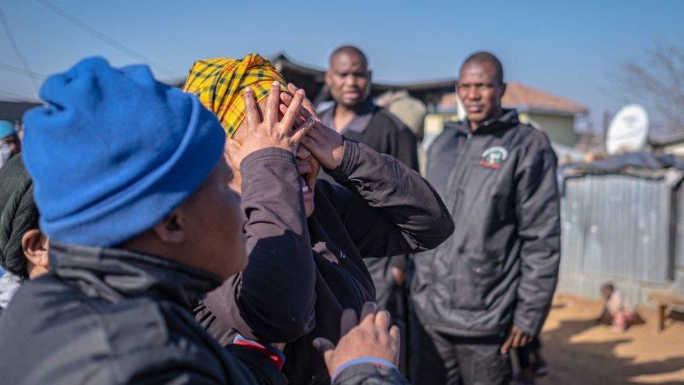 A relative of one of the victims shot dead in a tavern in Soweto reacts next to the crime scene in Soweto