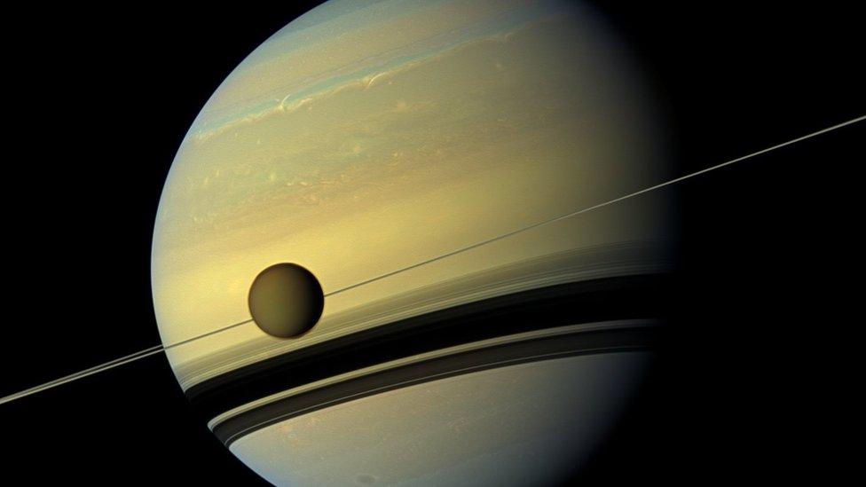 Saturn and its moon Titan. Titan's atmosphere is a featureless brown.