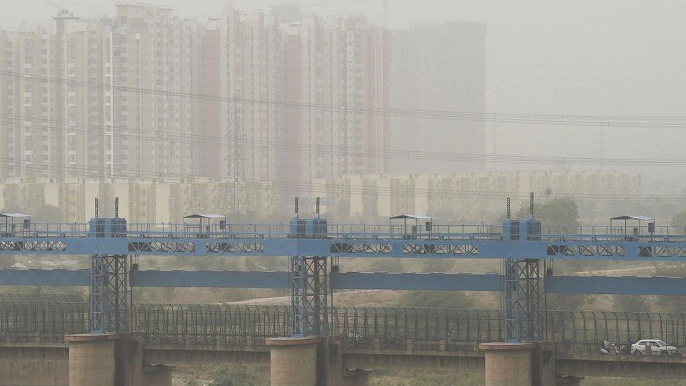 Vehicles cross a barrage on Hindon river as dust covers the skyline on the outskirts of New Delhi