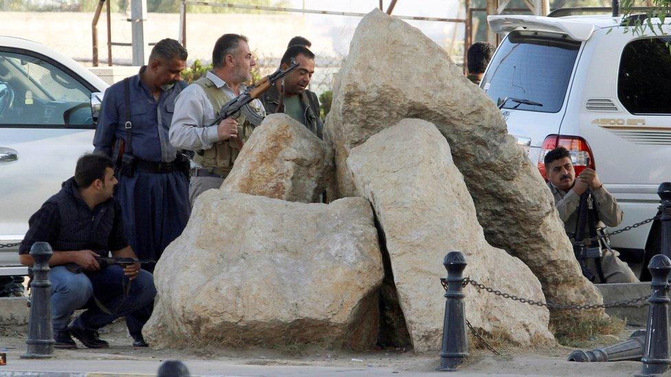 Men with guns standing behind rocks at a site of an attack by Islamic State militants in Kirkuk, Iraq, October 21, 2016.