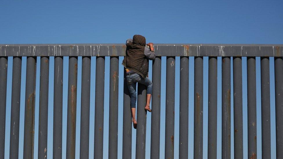 A migrant, part of a caravan of thousands from Central America trying to reach the United States, climbs the border fence