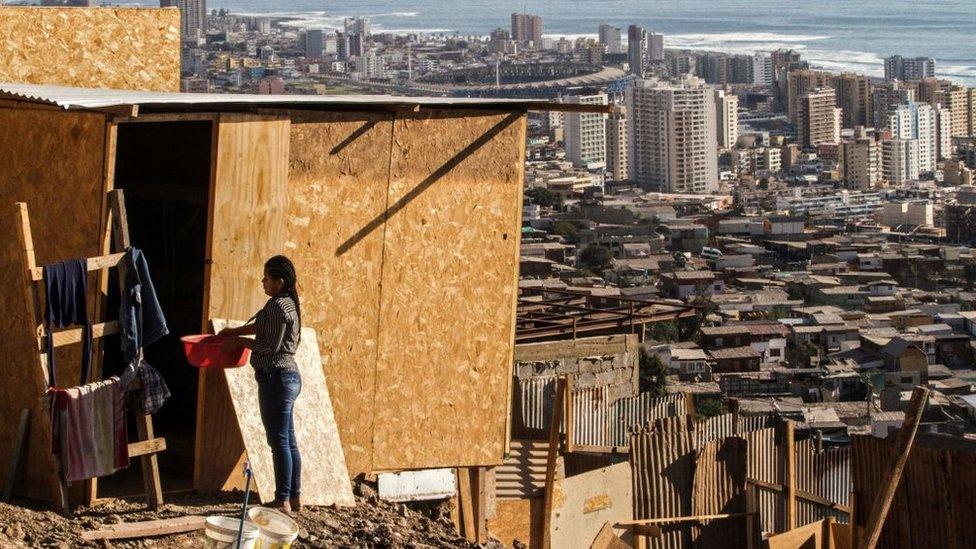 A woman stands outside her house at a camp in Altamira, Antofagasta, Chile, with the city of Antofagasta in the background, on 27 April