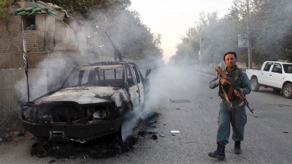 An Afghan policeman patrols next to a burning vehicle in the city of Kunduz