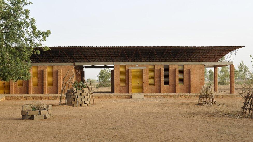 Gando Primary school. The building has many windows and yellow shutters. it has a flat roof.