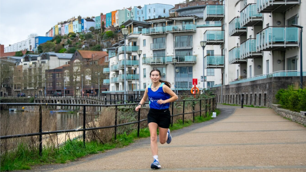 Ella runs by the harbour with Bristol's colourful houses behind her