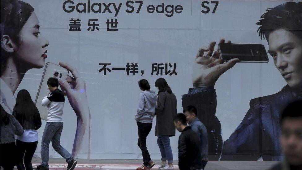 People walk past a poster at the entrance of a mall in Beijing