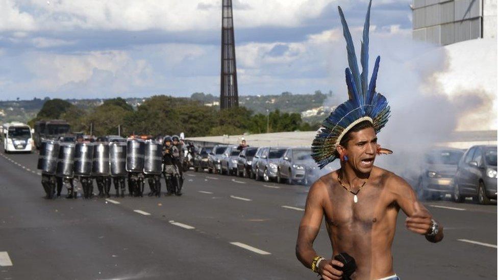 A member of an indigenous group stands before a group of riot police with shields during a land right protest in Brasilia on 25 April 2017