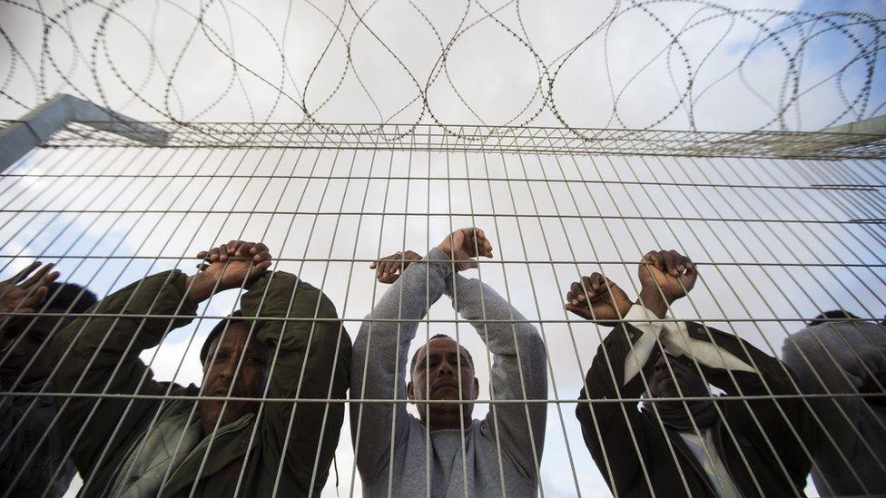 African asylum seekers, who entered Israel illegally via Egypt, lean at the fence of the Holot detention centre in Israel's southern Negev Desert, on February 17, 2014 as they join other migrants who came to protest outside the detention facility.