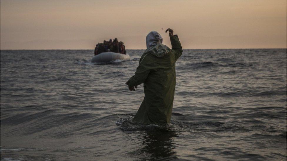 A volunteer gestures to refugees and migrants aboard a dinghy, as they approach a beach after crossing a part of the Aegean sea from the Turkey's coast to the north-eastern Greek island of Lesbos