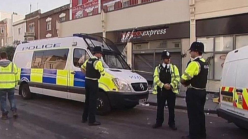 Police officers and riot vans outside damaged Tesco shop front