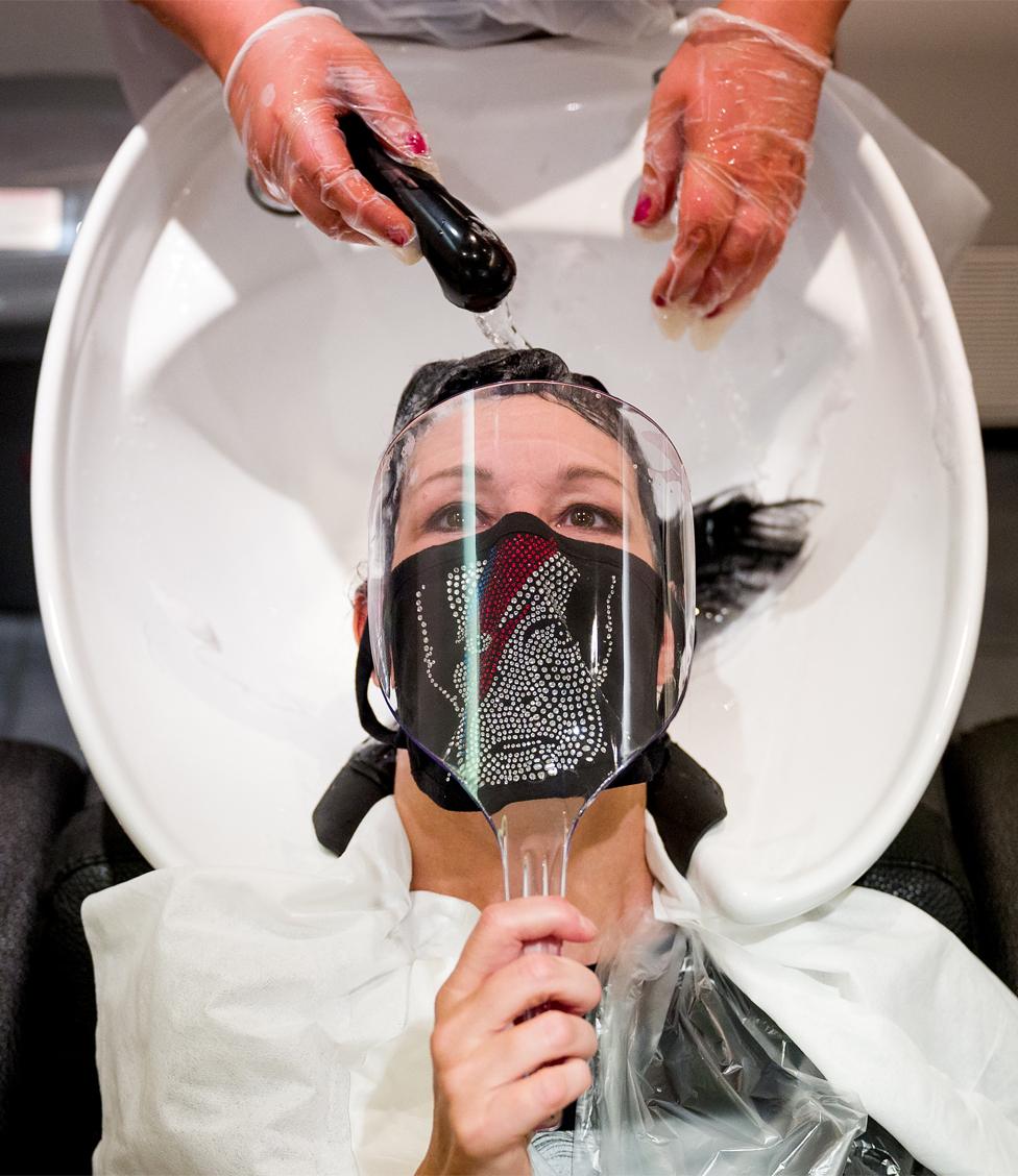 A customer wearing a face mask with David Bowie's face on has her hair washed in a hair salon