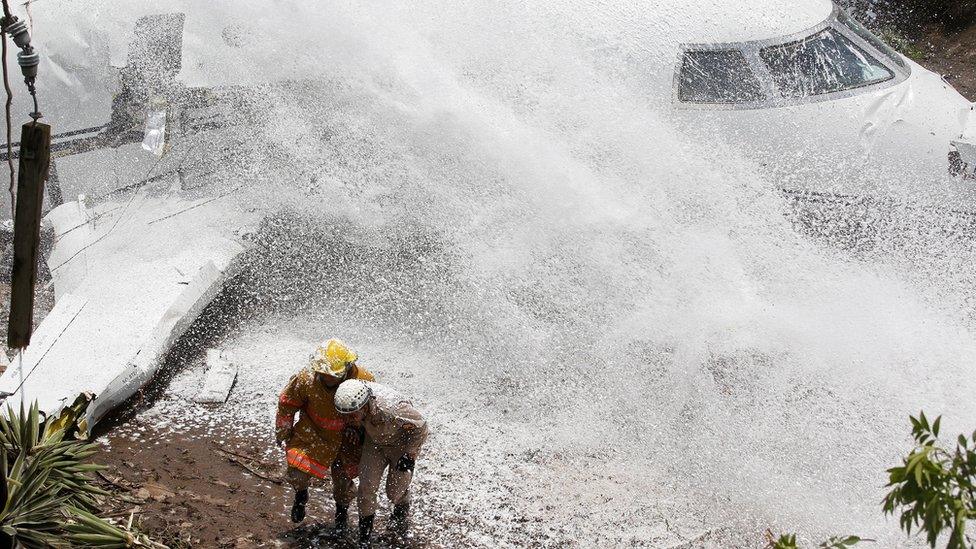 Firefighters take cover from firefighting foam applied onto the wreckage of a Gulfstream G200 aircraft that skidded off the runway during landing at Toncontin International Airport in Tegucigalpa, Honduras